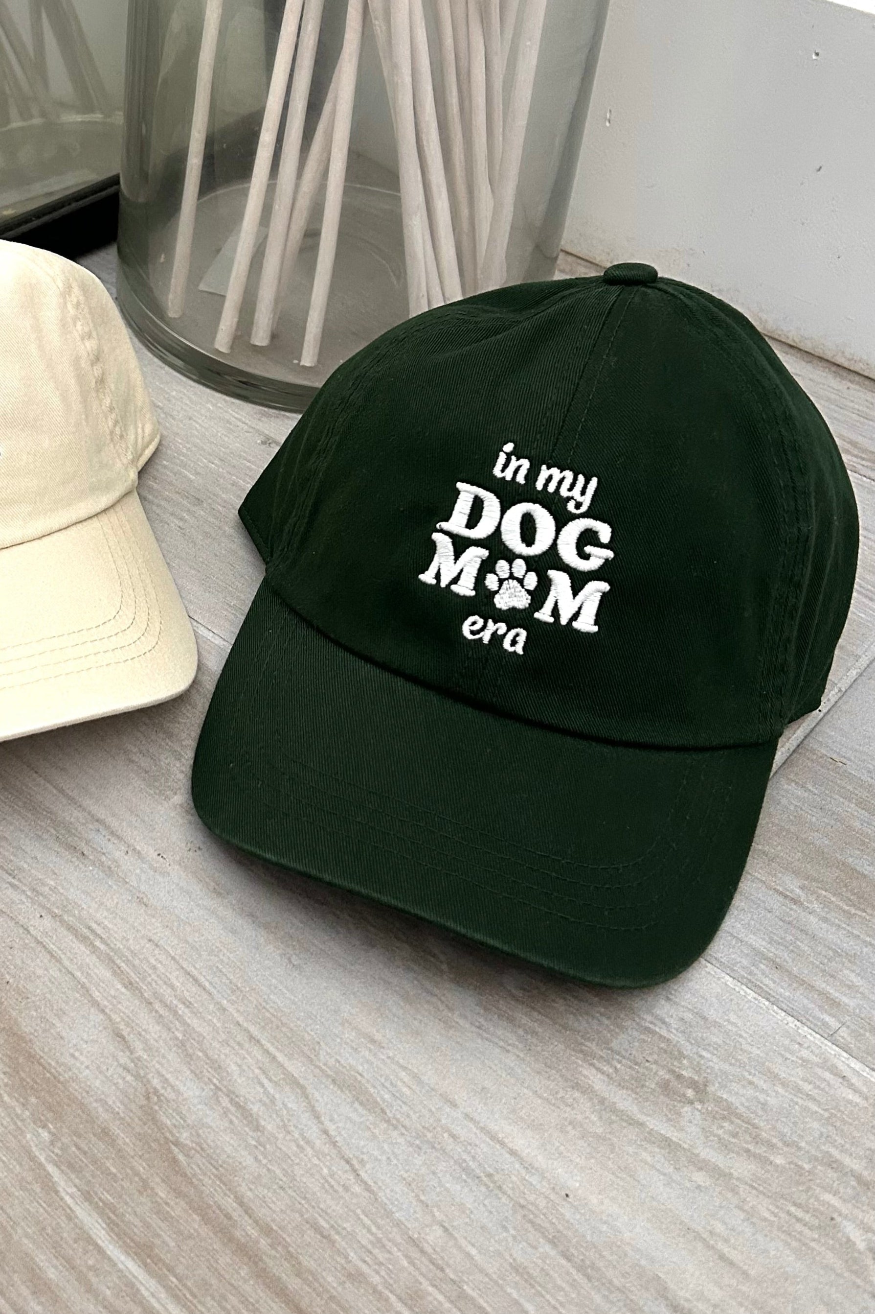 Get ready to represent all the dog moms out there with our Dog Mom Era Baseball Cap! Available in two color combinations - dark green with white letters or beige with maroon letters - and featuring an adjustable strap, this cap is both stylish and comfortable. One size fits all, so you can show off your love for your furry friend in the perfect fit.