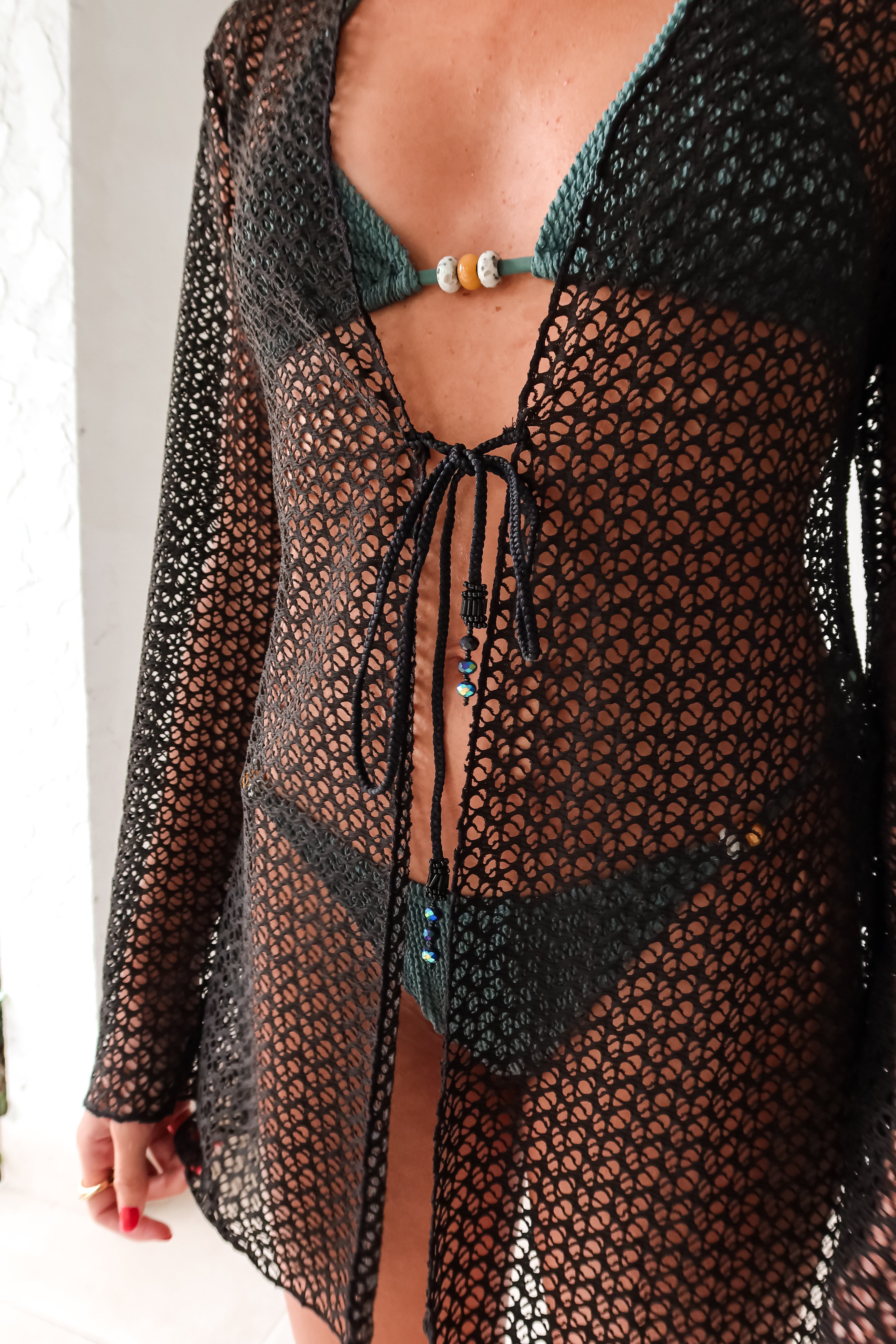 Cover up in style with our Newport Long Sleeve Tunic! This black tunic features a fashionable front tie closure and a beaded tie string detail, adding a touch of fun to your look. Perfect for layering, this tunic is a must-have for any wardrobe. Stay stylish and comfortable with this versatile piece.