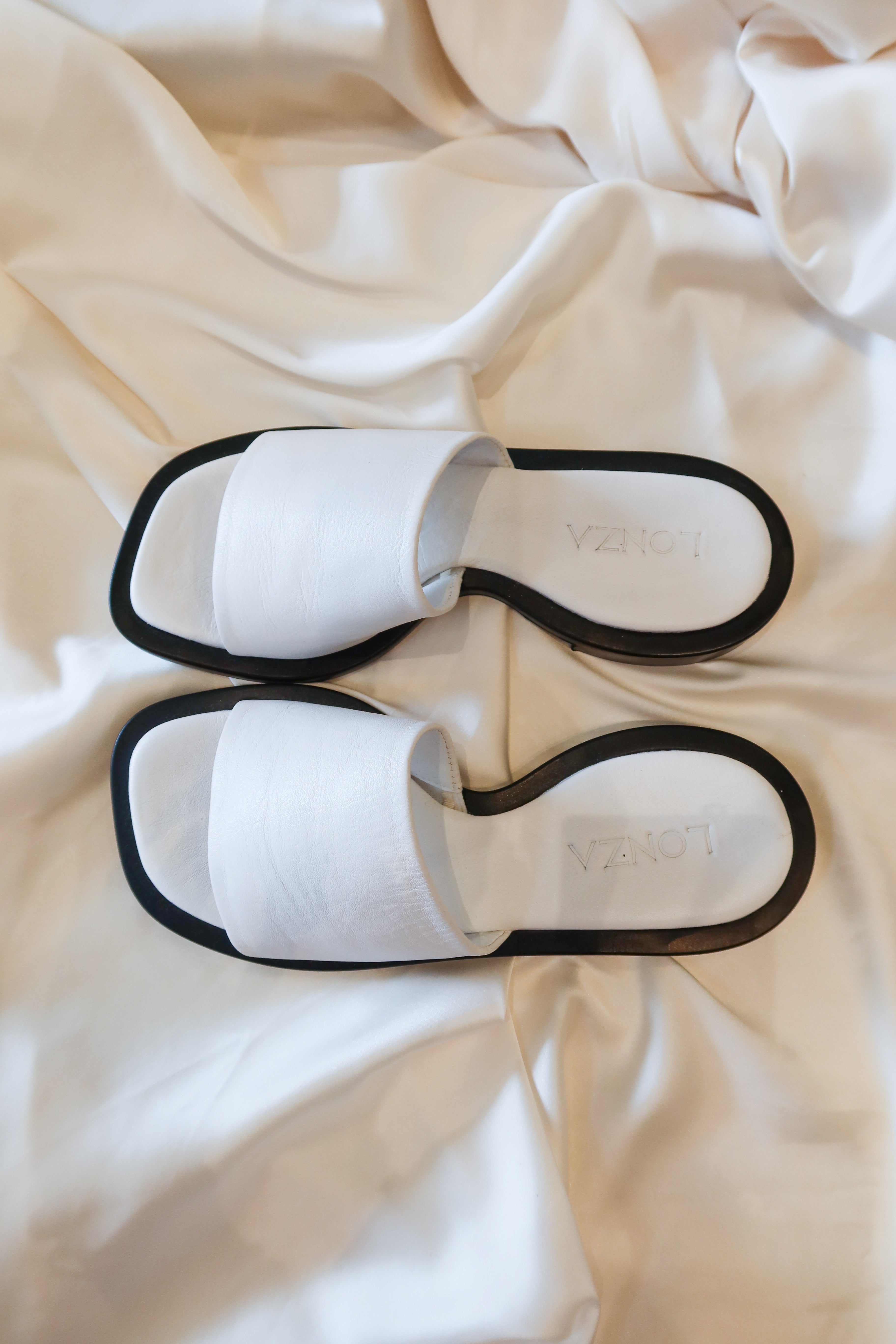 The LONZA LEATHER SANDAL: a white leather sandal with a comfortable fit. Perfect for strolling in style, these sandals boast a secure leather strap and will be your go-to choice for all-day comfort. Step out confidently with these sleek and stylish sandals!