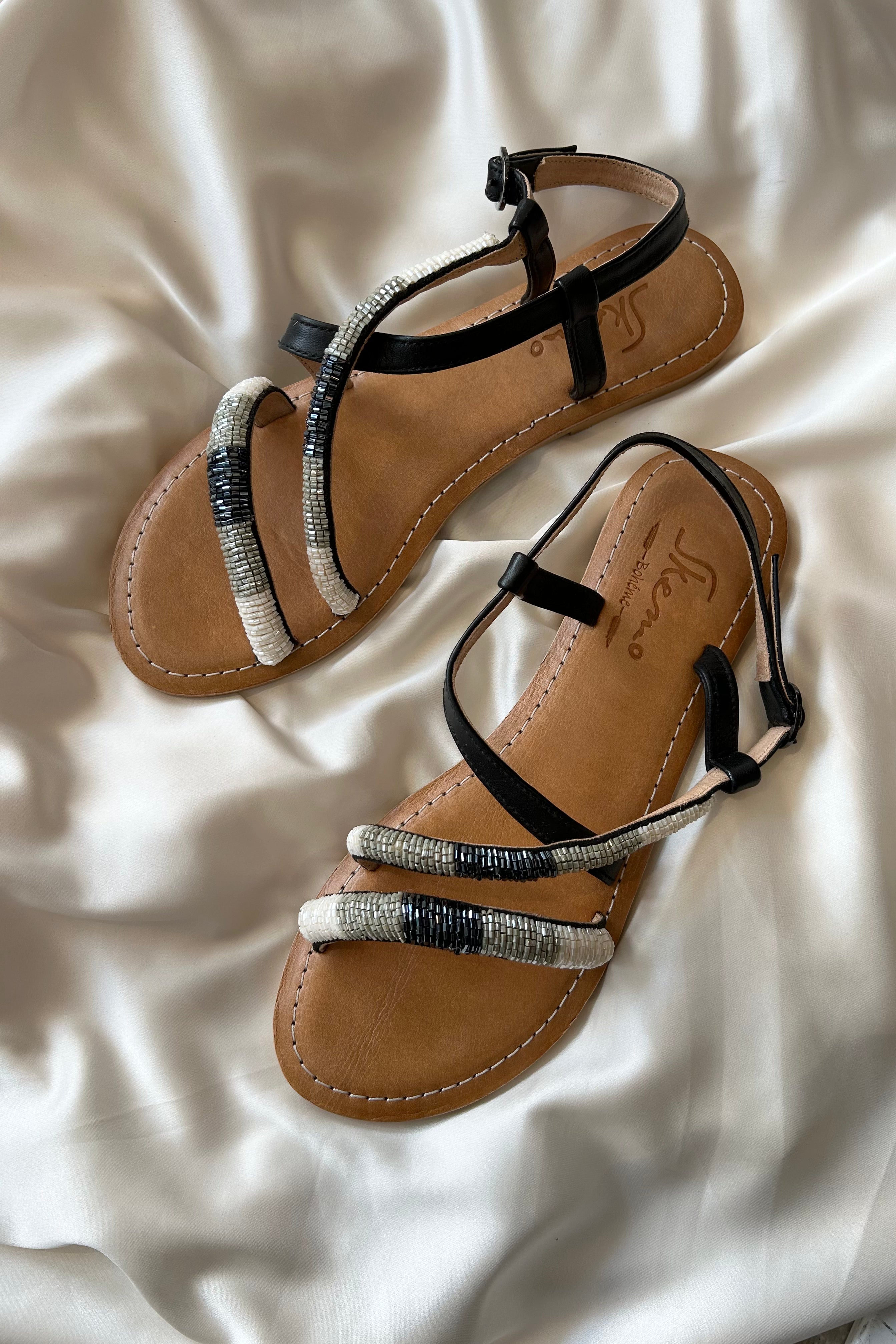 These cobra-inspired sandals take a bite out of boring footwear. Adorned with hand-beaded stripes in black, grey, and white, these leather sandals offer both style and comfort with a cushioned sole and adjustable side strap. Perfect for those who like to walk on the wild side.