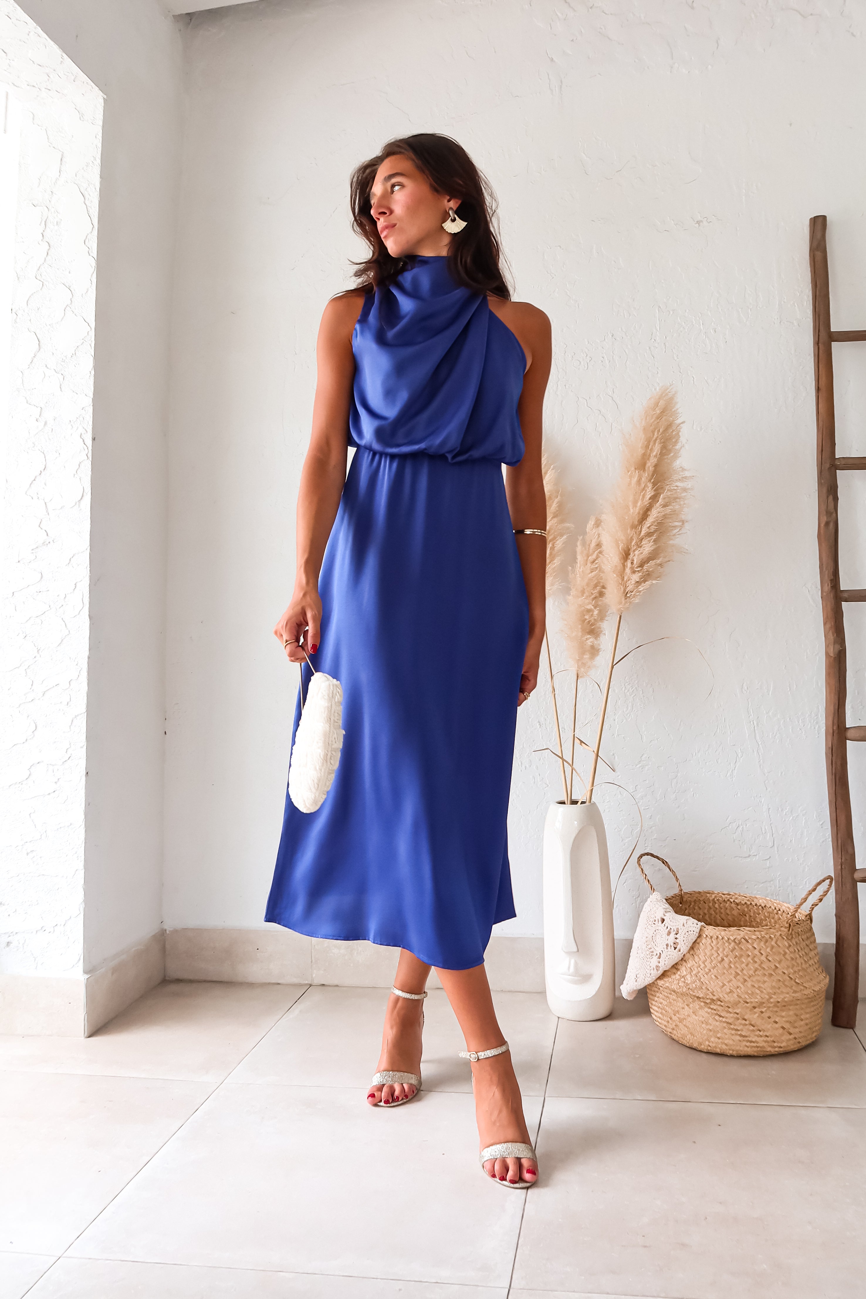 Indulge in luxurious comfort with the Bellagio Satin Maxi Dress in navy. The high neck and asymmetrical sleeveless top are accented with elegant buttons. The elastic scrunch torso and waist backing provide a comfortable fit, while the top is lined for added coverage.