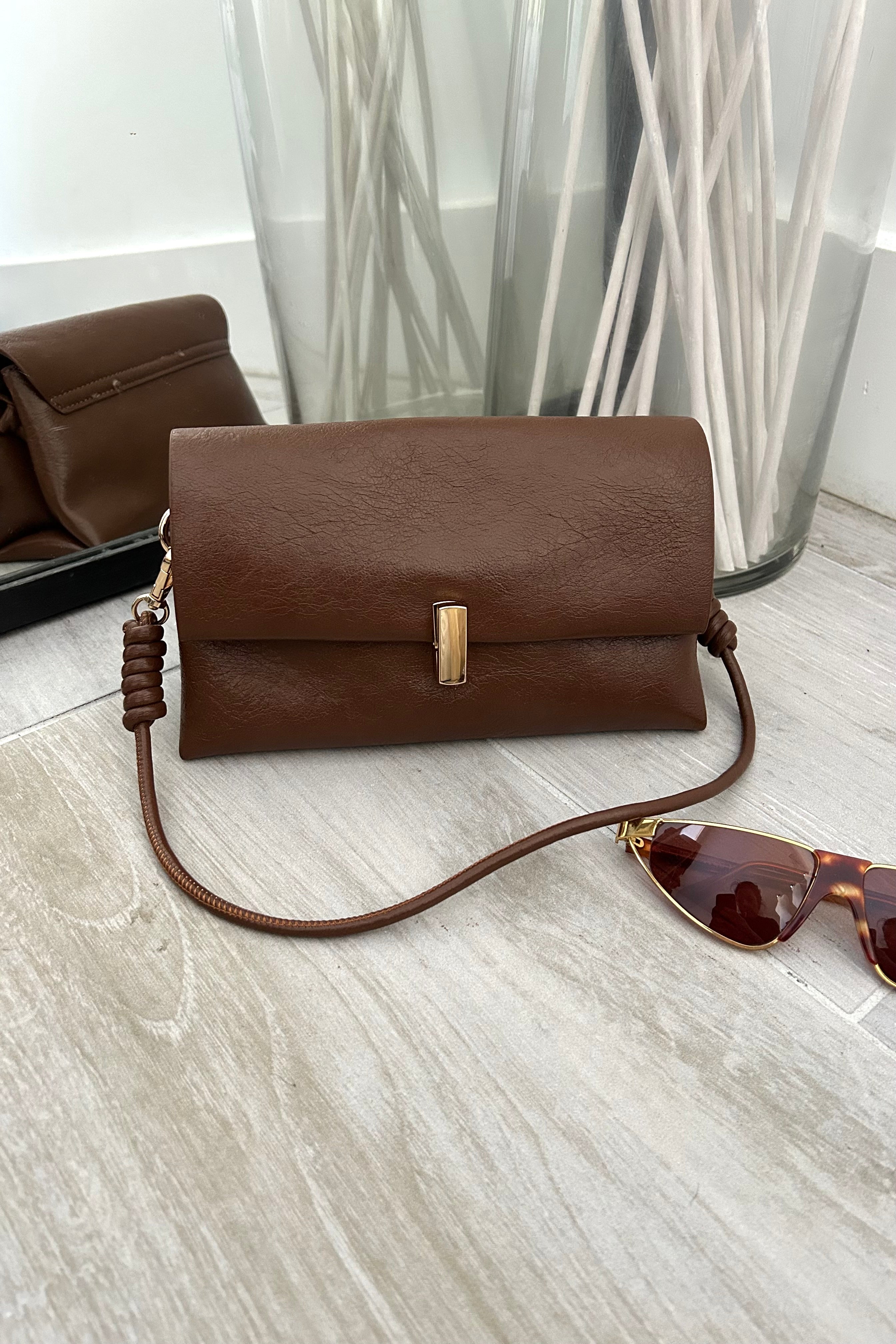 Introducing the LEXI PURSE - the perfect accessory for any outfit! Made with brown vegan leather, this purse is both stylish and sustainable. Carry it with ease thanks to the removable hand strap and secure your belongings with the gold buckle closure.&nbsp;