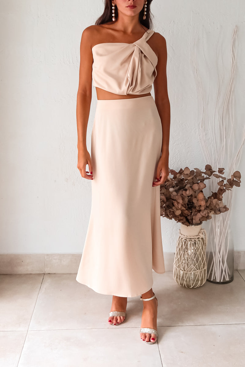 BRODEUX SATIN SKIRT SET! This luxe nude satin set features a one shoulder bubble crop top with a front twist detail, and a midi skirt with a side zipper closure and elastic band for a comfortable fit. Lined top and non-stretch material.