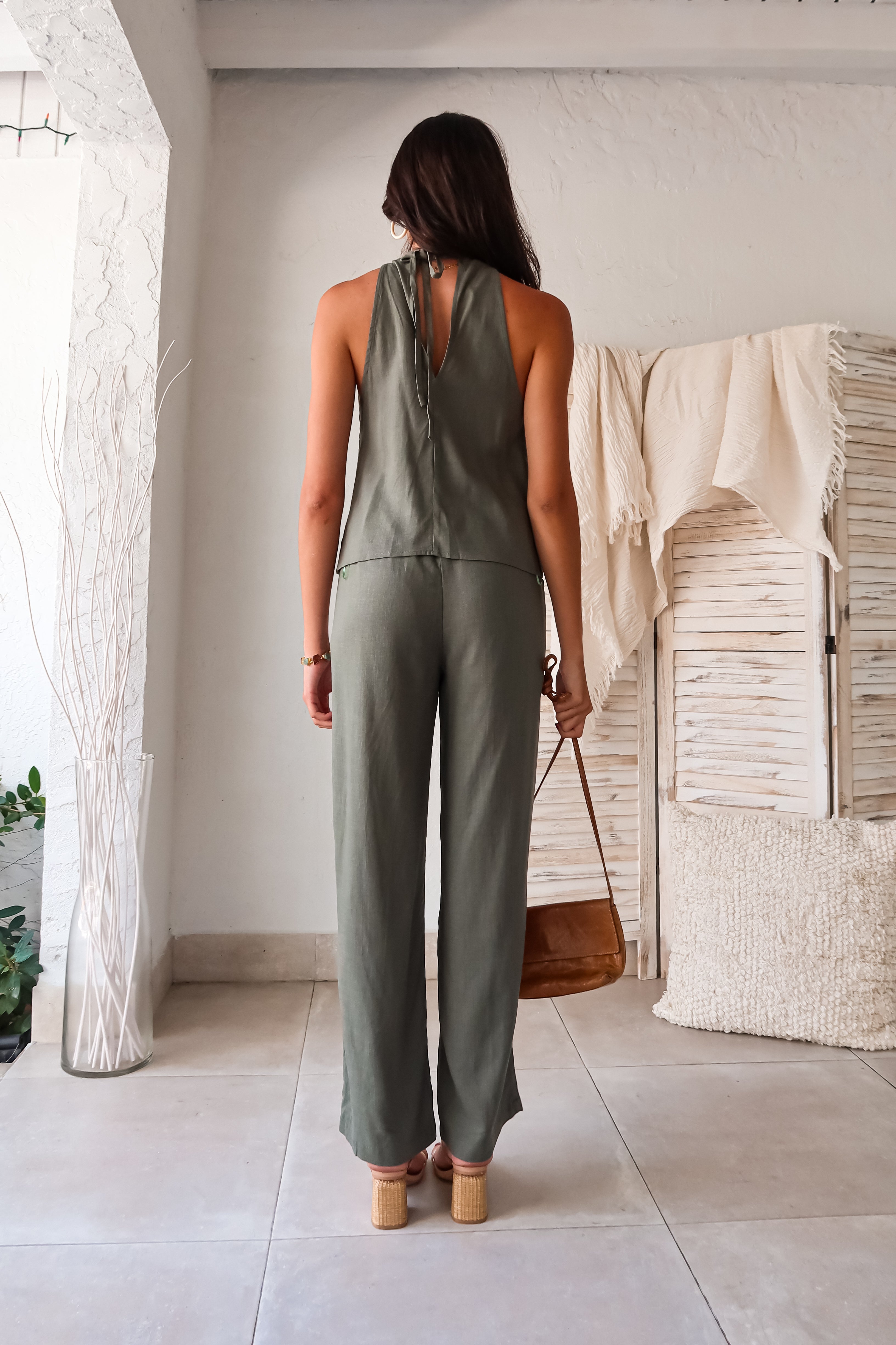 stylish in our Shoreline Linen Pant Set. This olive linen duo features a halter style top with a tie back and overlapping front for a unique touch. The elastic waistband and drawstring closure ensure a comfortable fit, while the front pockets add convenience. Perfect for warm weather,