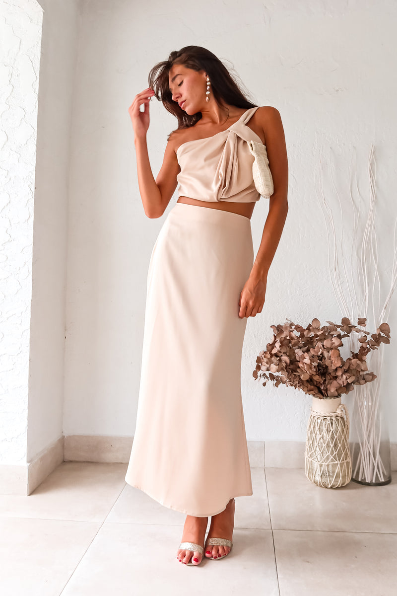 BRODEUX SATIN SKIRT SET! This luxe nude satin set features a one shoulder bubble crop top with a front twist detail, and a midi skirt with a side zipper closure and elastic band for a comfortable fit. Lined top and non-stretch material.