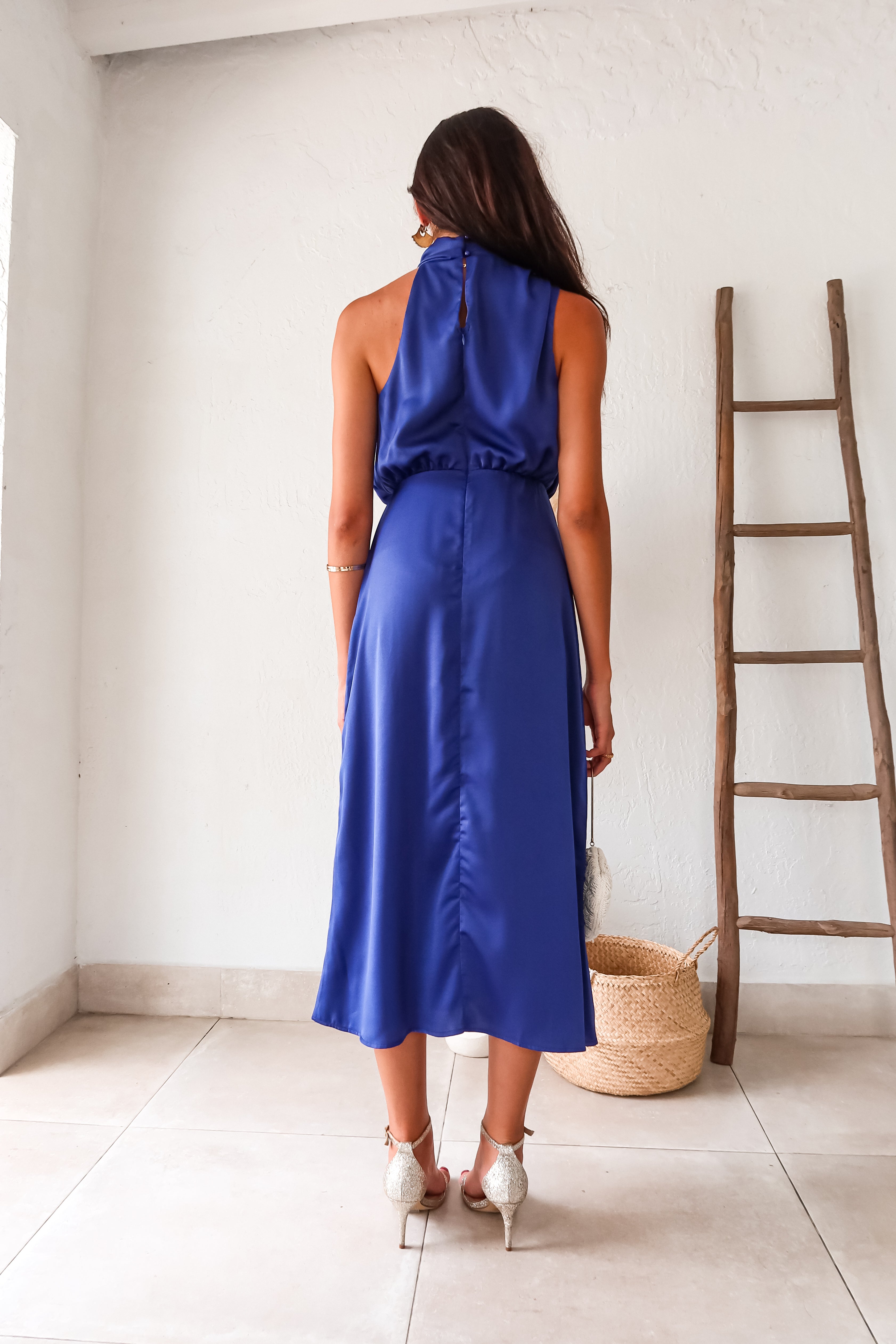 Indulge in luxurious comfort with the Bellagio Satin Maxi Dress in navy. The high neck and asymmetrical sleeveless top are accented with elegant buttons. The elastic scrunch torso and waist backing provide a comfortable fit, while the top is lined for added coverage.