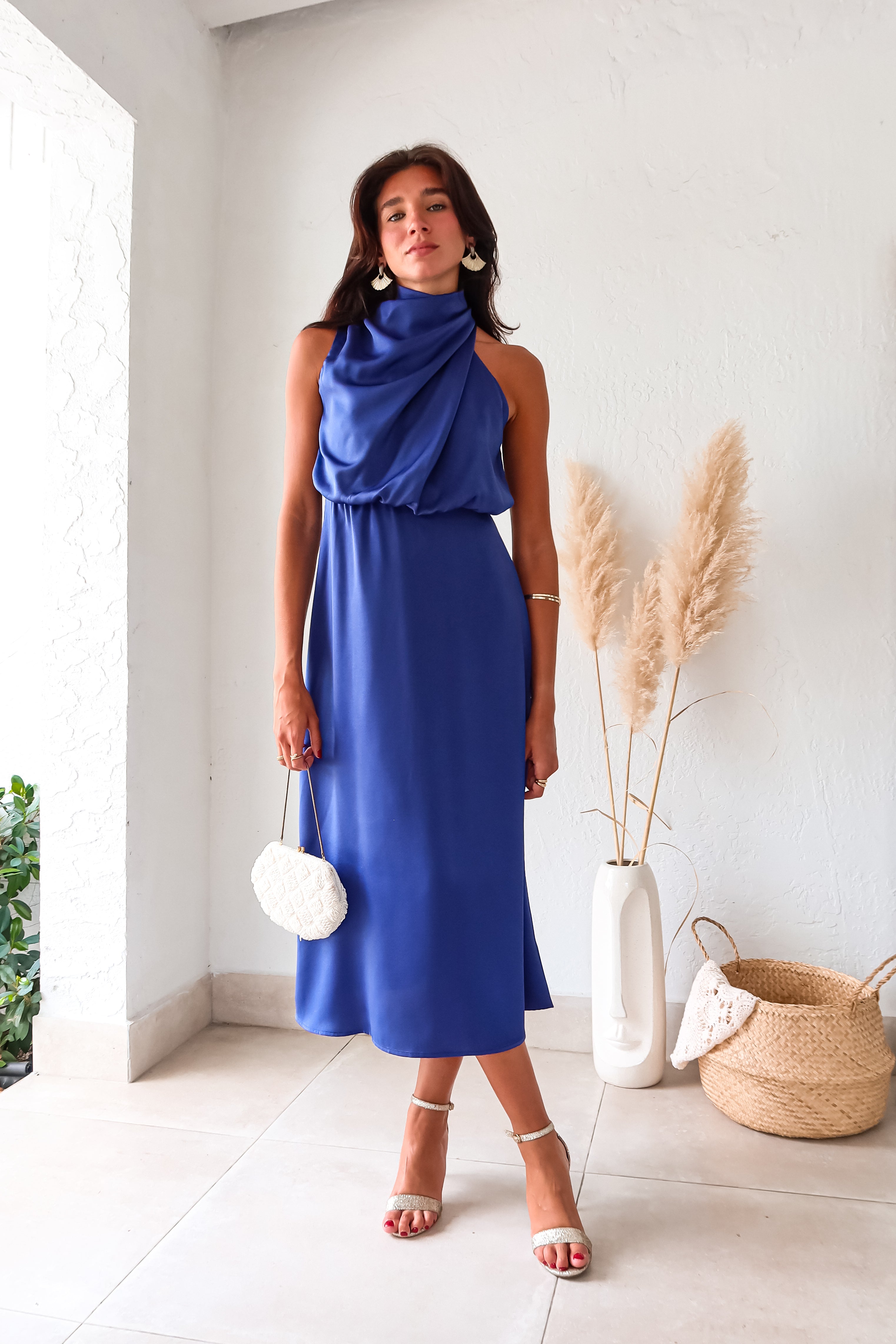 Indulge in luxurious comfort with the Bellagio Satin Maxi Dress in navy. The high neck and asymmetrical sleeveless top are accented with elegant buttons. The elastic scrunch torso and waist backing provide a comfortable fit, while the top is lined for added coverage.