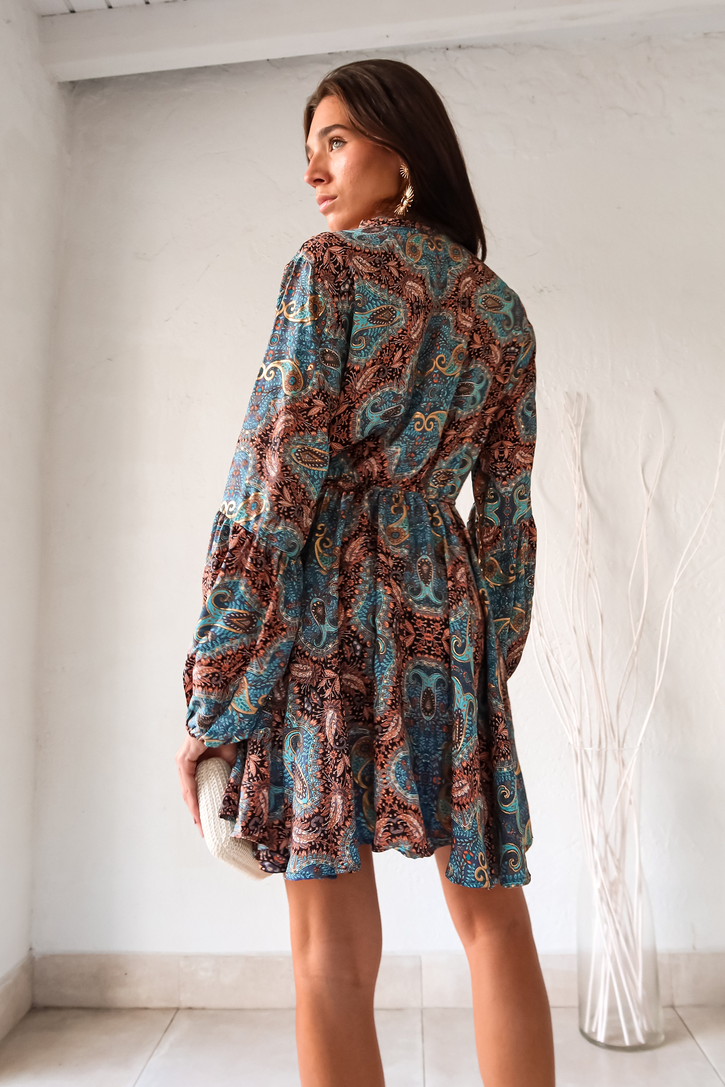 Add some playful flair to your wardrobe with our Barcelona Long Sleeve Mini Dress! Featuring a vibrant turquoise, gold, black, and orange floral paisley design, this dress will surely turn heads. The long sleeves with bubble wrists and front button closure with waist tie string add unique touches to this one-of-a-kind piece.