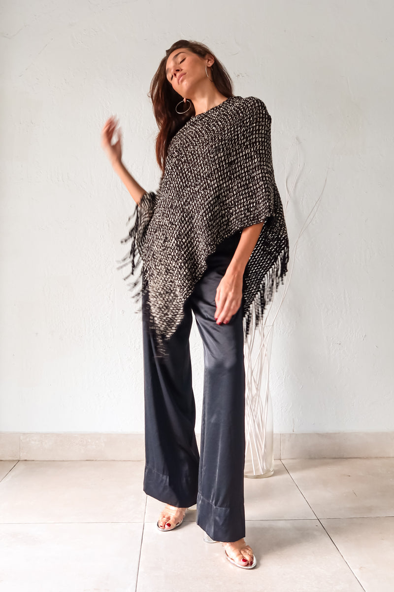 Embrace your wild side with our FULL MOON LUREX PONCHO. The black lurex sweater poncho features silver fabric detailing, a fringed bottom, and stretchy fabric for a comfortable fit that flatters any size. Perfect for a night out or cozying up by the fire. One size fits XS-L.