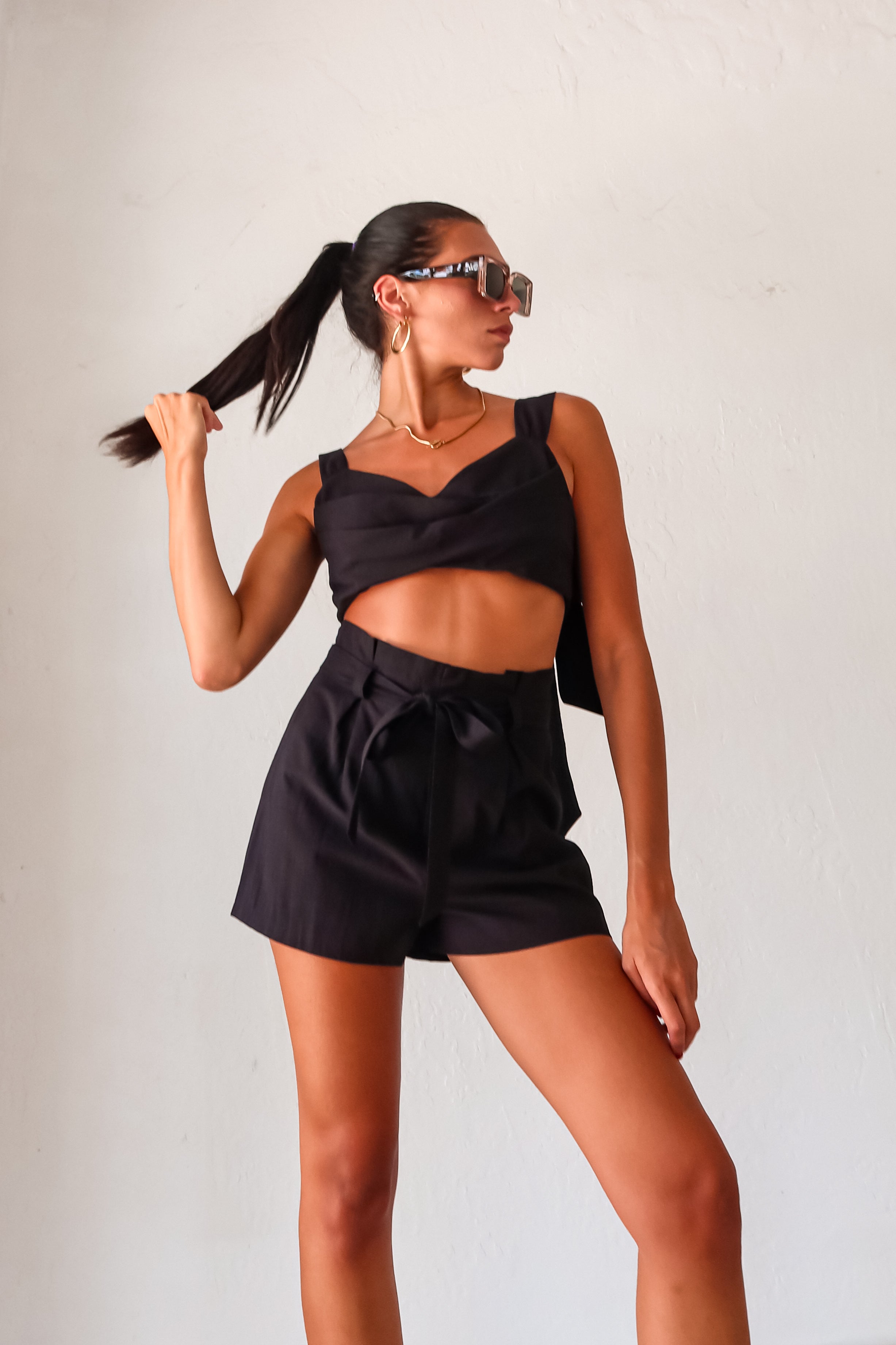 the Always On Time Short Set! This black linen crop top and pleated shorts combo is both stylish and functional. With a cowl bust and adjustable bow tie straps, you can easily customize your fit. Plus, the back zipper and optional tie belt make dressing a breeze.