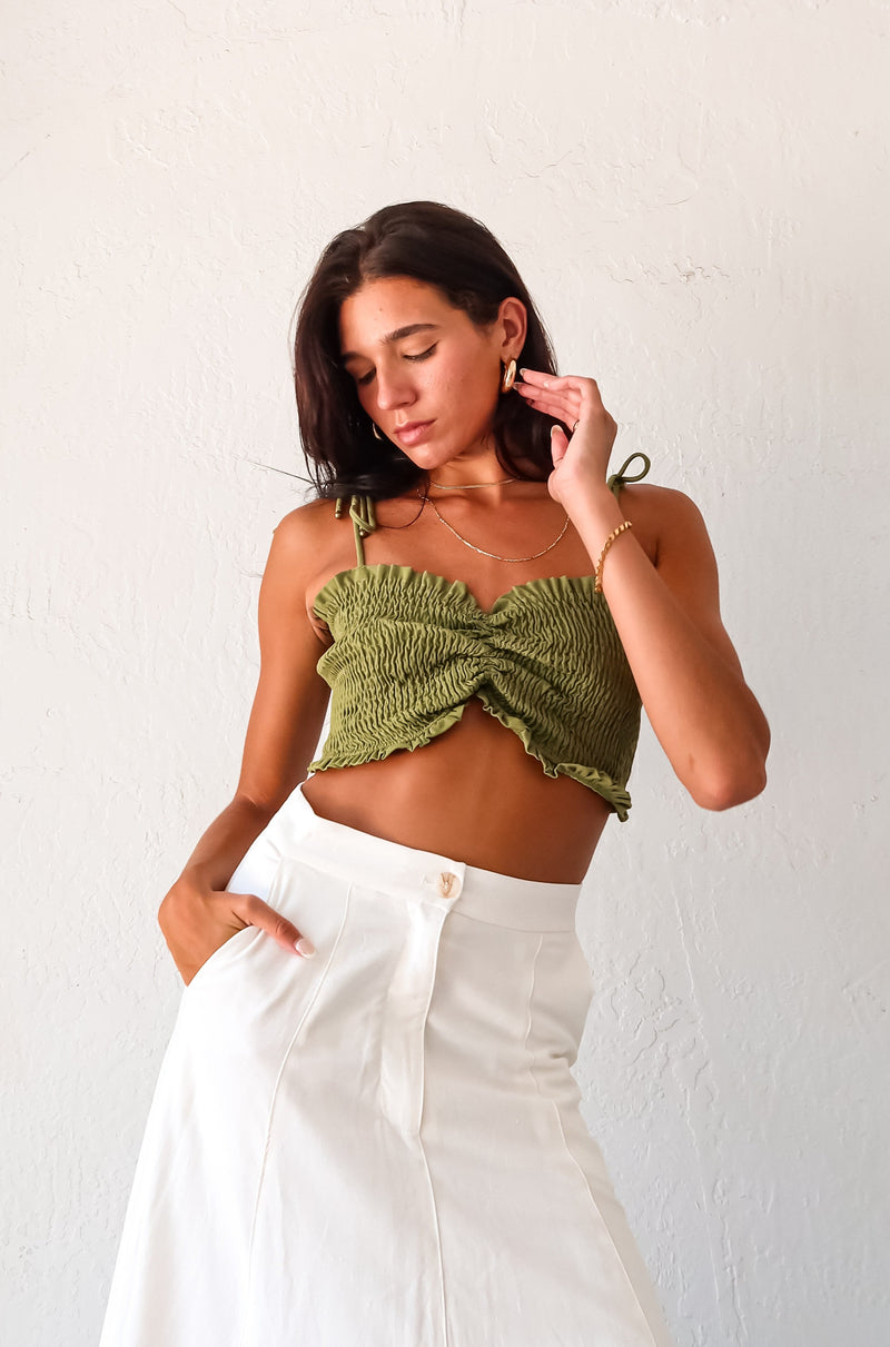 Get ready to turn heads in our ARCADIA SMART CROP TOP! This playful olive green crop top features a criss cross front design and smocked fabric, providing a comfortable stretchy fit. With ruffled edges and adjustable shoulder straps, this non-lined top is perfect for a fun night out! Pair with the Misommar Linen Maxi Skirt for a complete look.