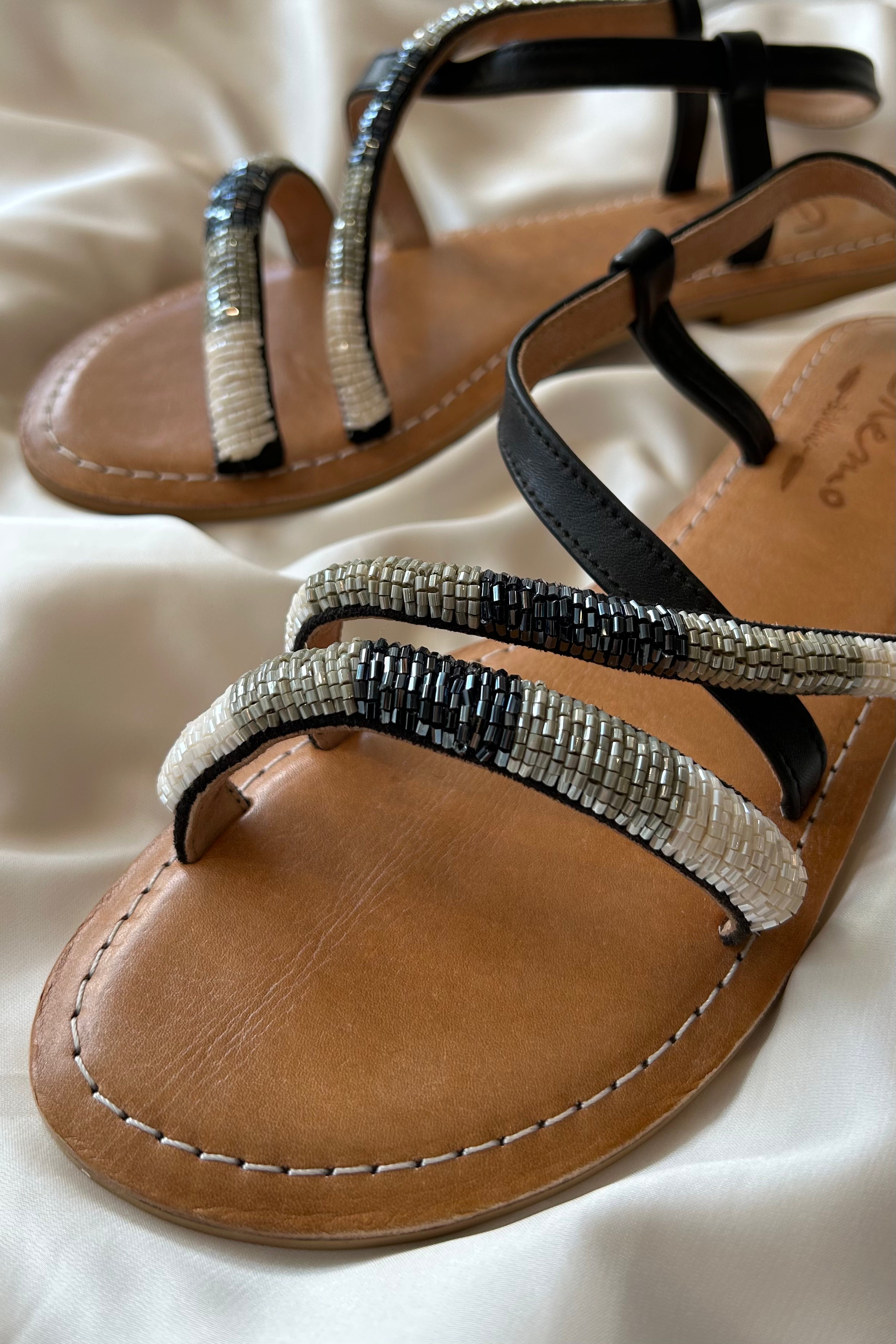 These cobra-inspired sandals take a bite out of boring footwear. Adorned with hand-beaded stripes in black, grey, and white, these leather sandals offer both style and comfort with a cushioned sole and adjustable side strap. Perfect for those who like to walk on the wild side.