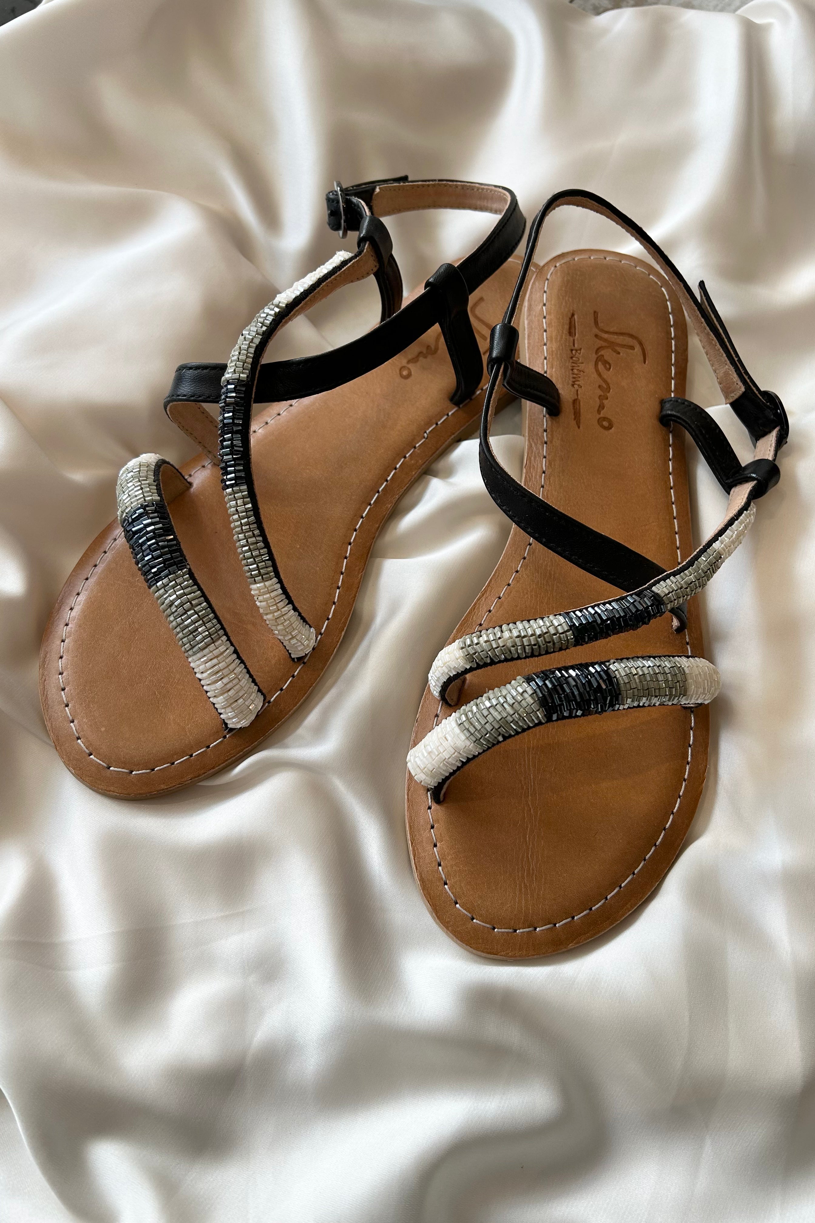 These cobra-inspired sandals take a bite out of boring footwear. Adorned with hand-beaded stripes in black, grey, and white, these leather sandals offer both style and comfort with a cushioned sole and adjustable side strap. Perfect for those who like to walk on the wild side.