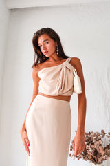 BRODEUX SATIN SKIRT SET! This luxe nude satin set features a one shoulder bubble crop top with a front twist detail, and a midi skirt with a side zipper closure and elastic band for a comfortable fit. Lined top and non-stretch material.