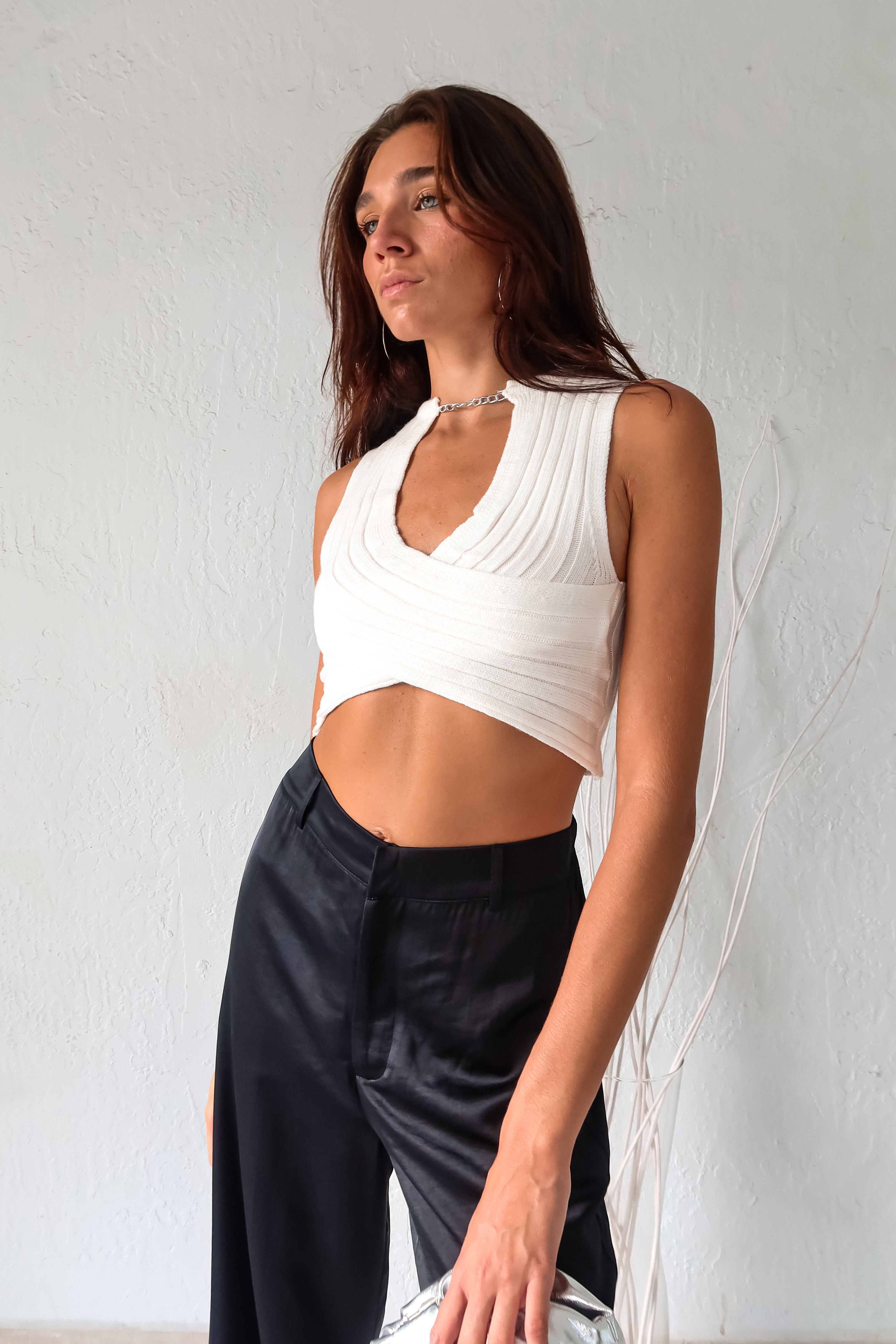 Add some edge to your wardrobe with our white ribbed crop top! Featuring a unique neck chain detail and front overlap design, this top is sure to turn heads. The stretchy fabric ensures a comfortable fit for all-day wear.