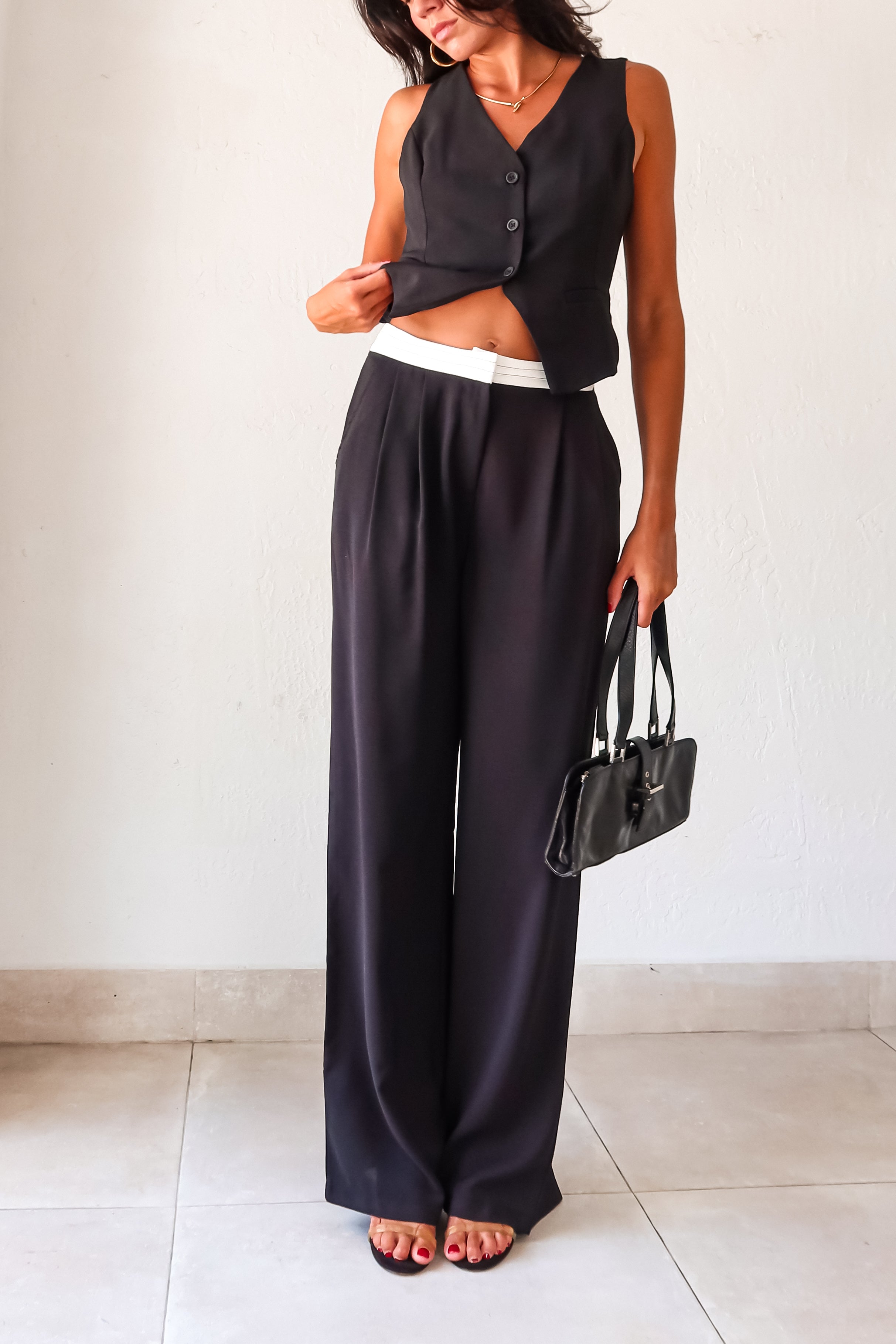 The Melrose Place Vest Pant Set is the perfect combination of style and quirkiness. The black vest and pants feature unique details such as an open back with adjustable buckle silver detail, front button closure, and pleated pants with a white detail waist. Stay comfortable and trendy 