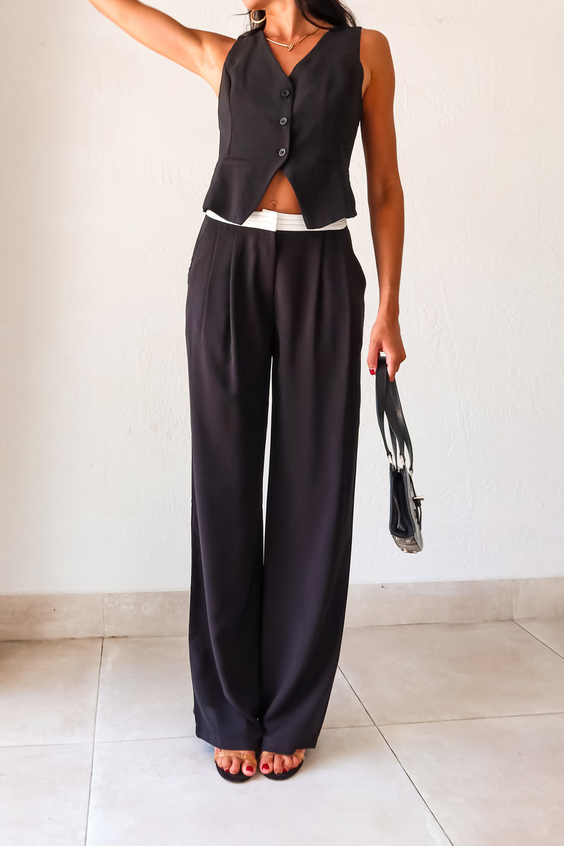 The Melrose Place Vest Pant Set is the perfect combination of style and quirkiness. The black vest and pants feature unique details such as an open back with adjustable buckle silver detail, front button closure, and pleated pants with a white detail waist. Stay comfortable and trendy 