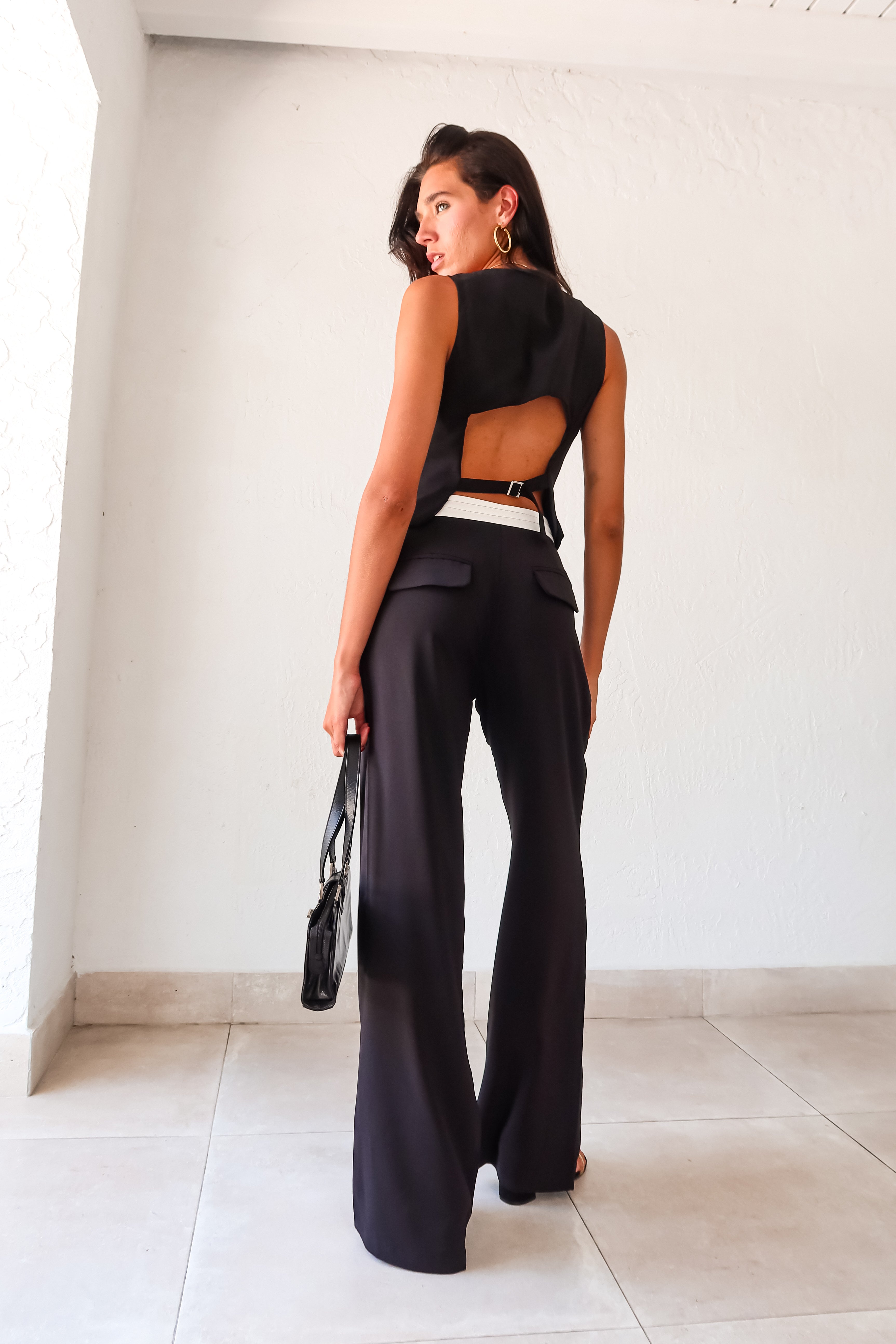 The Melrose Place Vest Pant Set is the perfect combination of style and quirkiness. The black vest and pants feature unique details such as an open back with adjustable buckle silver detail, front button closure, and pleated pants with a white detail waist. Stay comfortable and trendy 