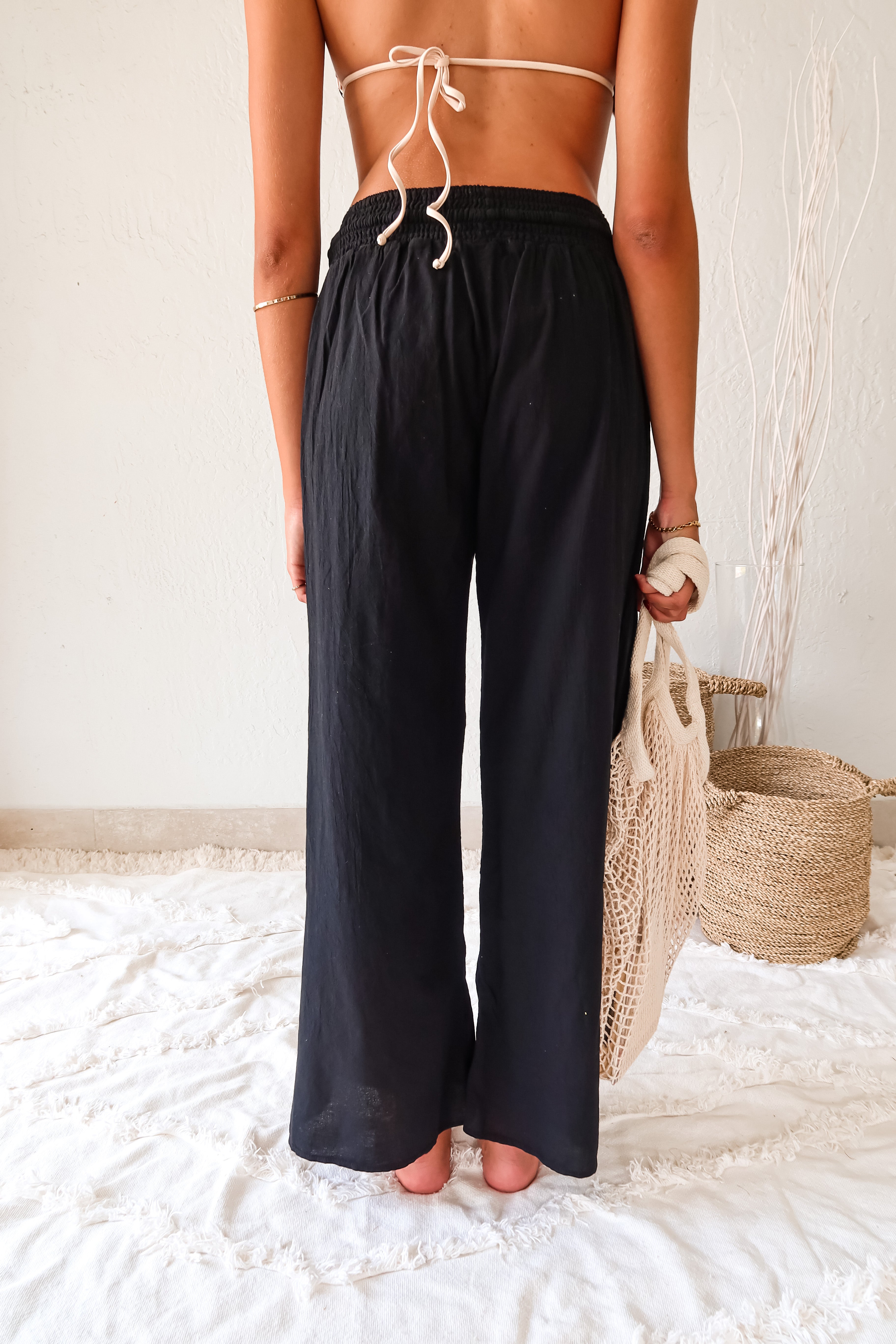 Add a touch of playfulness to your beach look with the CATALINA PANT. These black linen slit pants feature a smocked waist with an adjustable drawstring tie for a comfortable fit. The double leg high slit adds a unique touch, while its one size fits all design makes it a versatile addition to your wardrobe. Hand wash cold and pair with our Azusa/Cerritos reversible kenya print bikini set for a fun look.