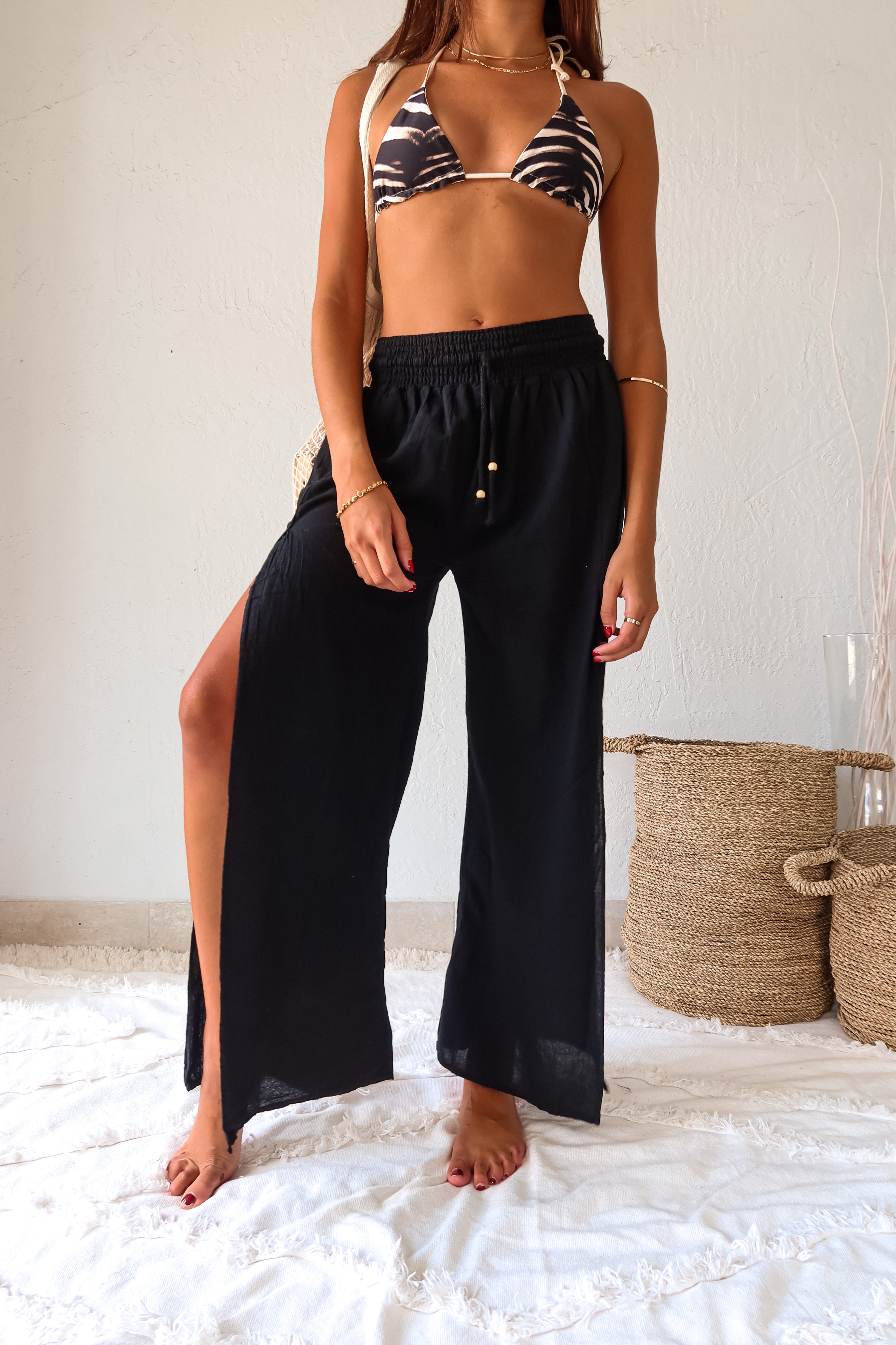 Add a touch of playfulness to your beach look with the CATALINA PANT. These black linen slit pants feature a smocked waist with an adjustable drawstring tie for a comfortable fit. The double leg high slit adds a unique touch, while its one size fits all design makes it a versatile addition to your wardrobe. Hand wash cold and pair with our Azusa/Cerritos reversible kenya print bikini set for a fun look.