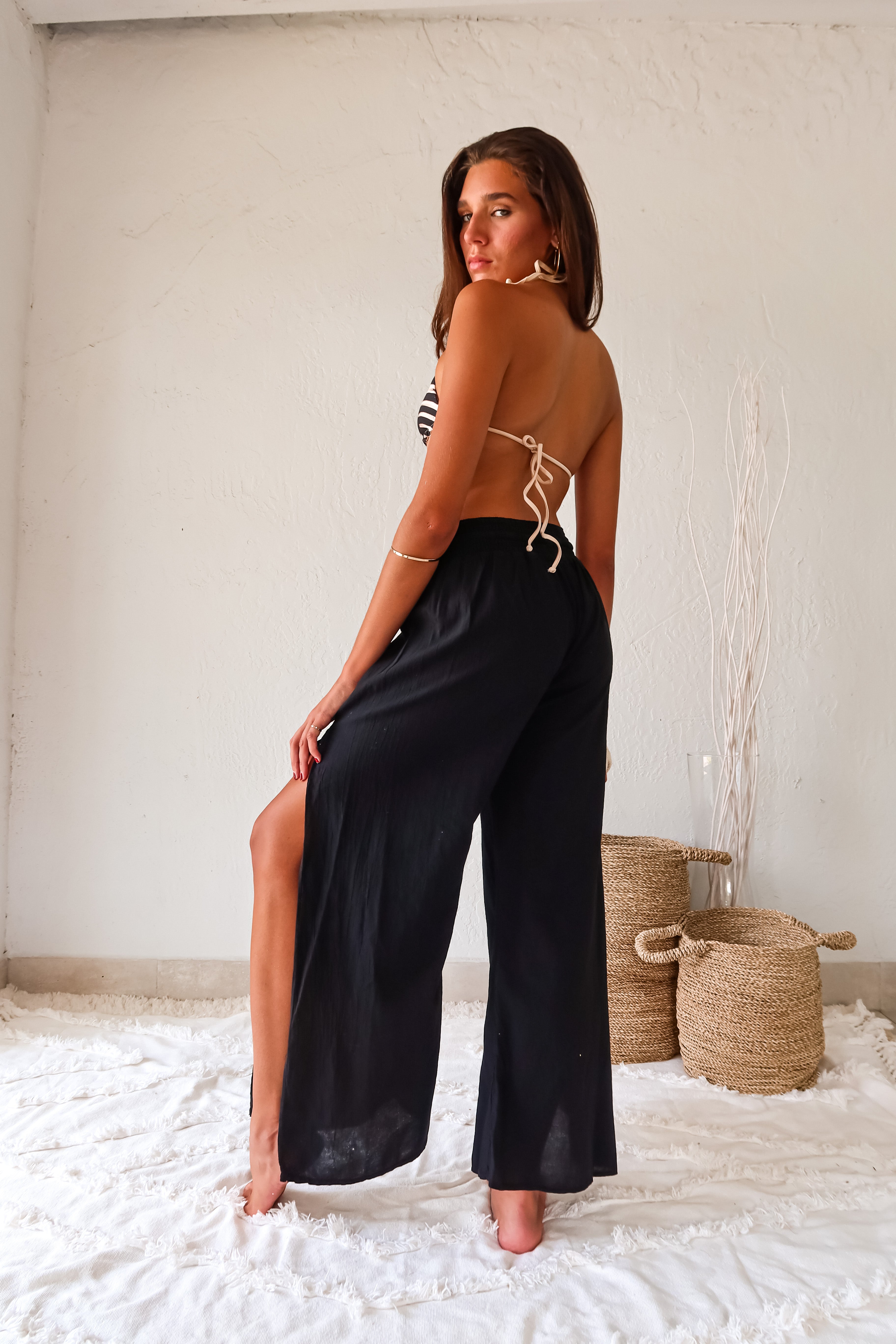 Add a touch of playfulness to your beach look with the CATALINA PANT. These black linen slit pants feature a smocked waist with an adjustable drawstring tie for a comfortable fit. The double leg high slit adds a unique touch, while its one size fits all design makes it a versatile addition to your wardrobe. Hand wash cold and pair with our Azusa/Cerritos reversible kenya print bikini set for a fun look.